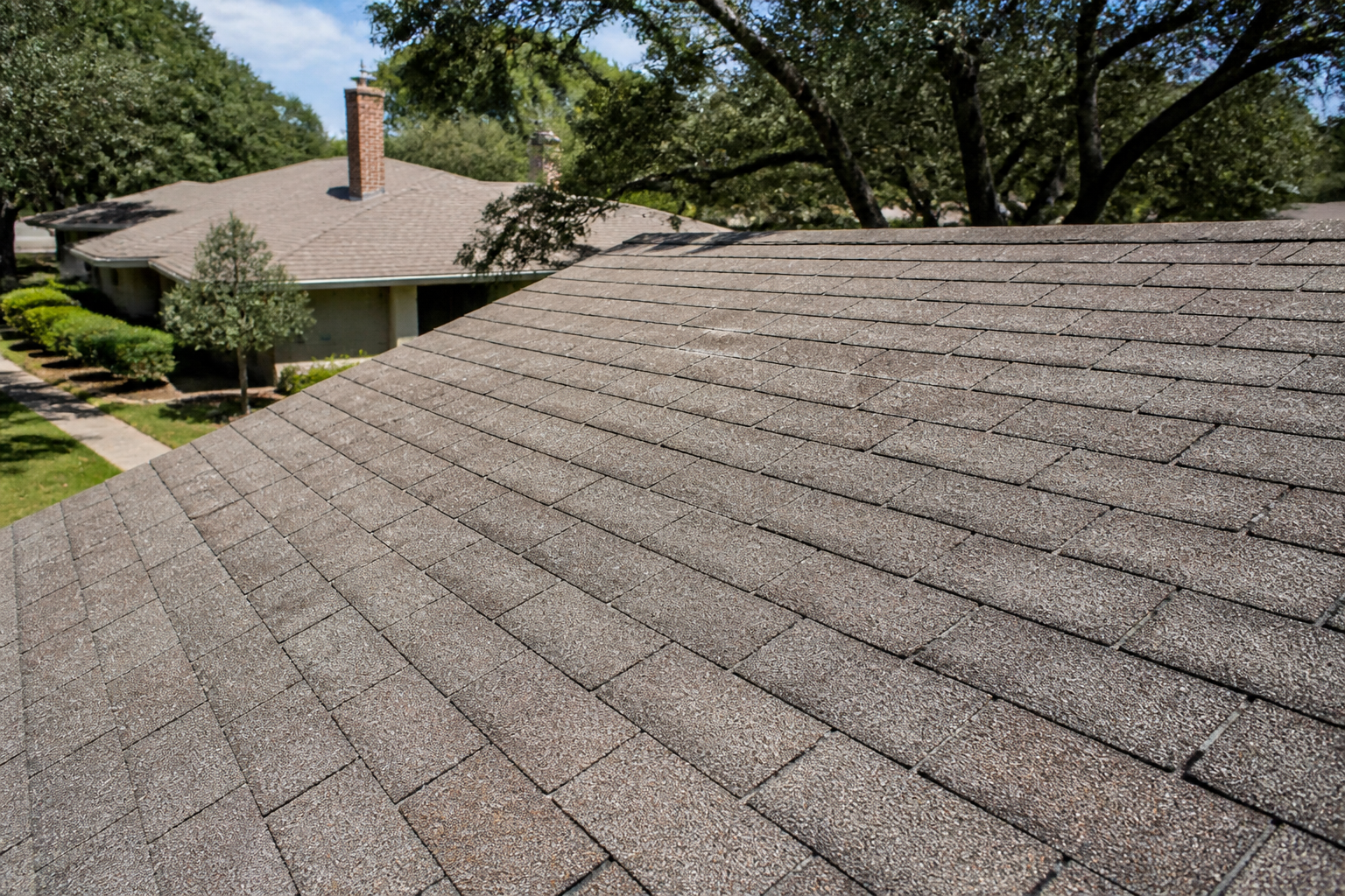 Close-up of sun-damaged asphalt shingles on a San Antonio home, showing granule loss and cracks from UV exposure.